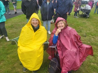 Two ladies sitting in Ponchos in a field.